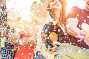 Happy friends having fun at festival party throwing confetti and